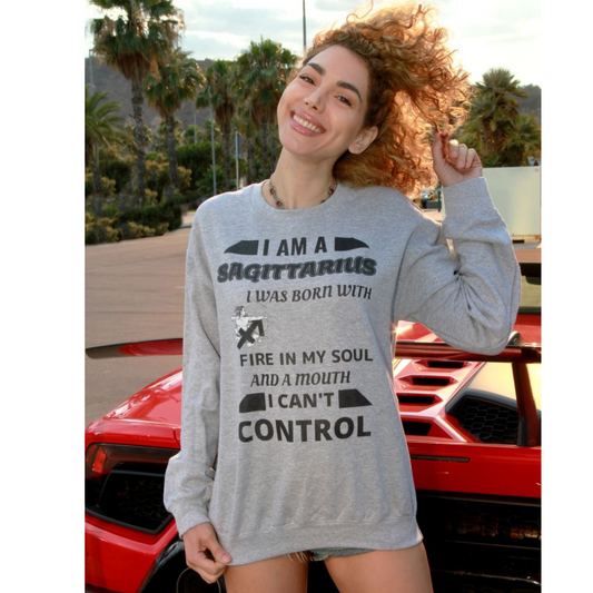 Woman wearing grey Sagittarius zodiac sweatshirt with bold quote – I was born with fire in my soul and a mouth I can’t control – standing in front of red sports car, casual astrology-themed fashion.
